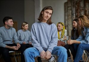 young man sitting in the center of other young people engaged in a group therapy program