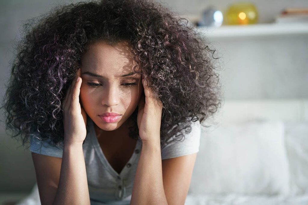 teenage woman sitting on her bed and holding her head in her hands because she feels that understanding anxiety and teens is impossible