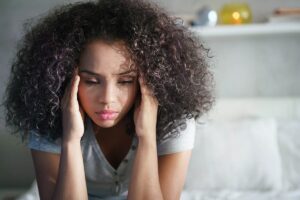 teenage woman sitting on her bed and holding her head in her hands because she feels that understanding anxiety and teens is impossible